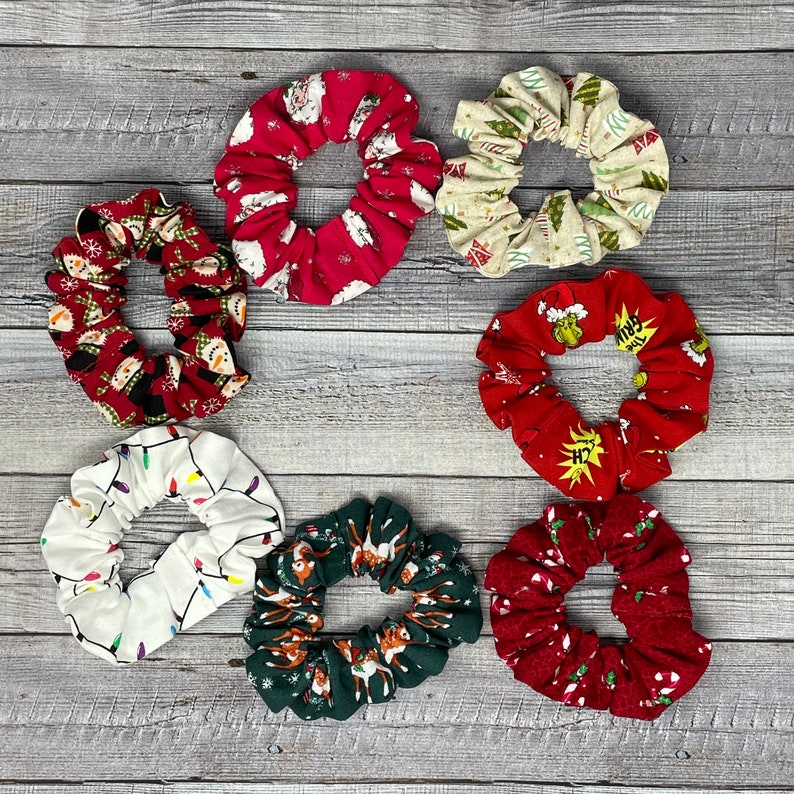 K&ouml;nnte beinhalten: Set mit 8 Weihnachts-Haargummis in verschiedenen Farben und Mustern, darunter Rot, Gr&uuml;n, Wei&szlig; und Creme. Die Haargummis zeigen Weihnachtsmotive wie Weihnachtsmann, Rentier, Lichter und Grinch.