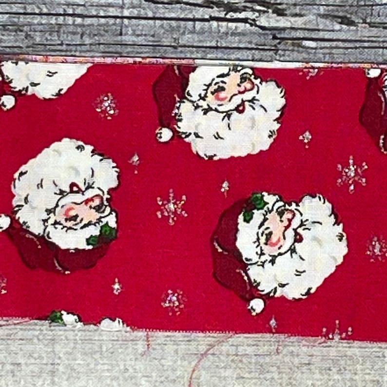 K&ouml;nnte beinhalten: Roter Stoff mit einem sich wiederholenden Muster aus wei&szlig;en Weihnachtsmann-Gesichtern. Der Stoff hat eine glitzernde Textur.