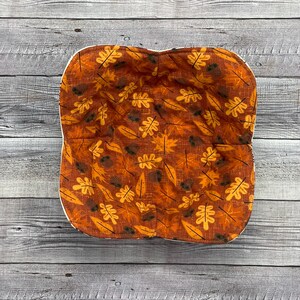 May include: A brown and orange fabric bread bowl with a white trim and a pattern of leaves and acorns.