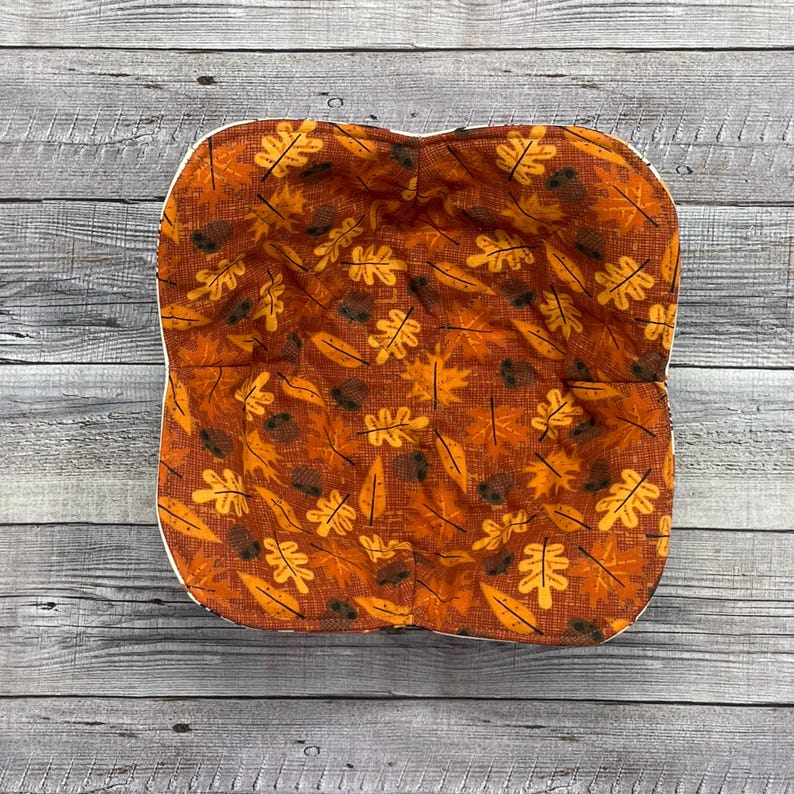May include: A brown and orange fabric bread bowl with a white trim and a pattern of leaves and acorns.