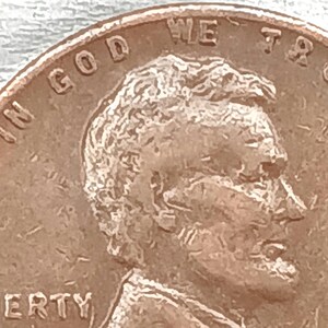 Puede incluir: Primer plano de un centavo de cobre con las palabras "IN GOD WE TRUST" y "LIBERTY" visibles. El perfil de Abraham Lincoln aparece en la moneda.
