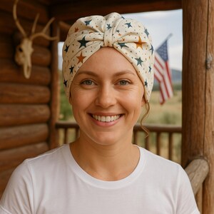 Peut inclure: Une femme portant un turban blanc avec des étoiles brunes et bleues. Le turban est noué sur le dessus de sa tête. Elle sourit et porte un t-shirt blanc.