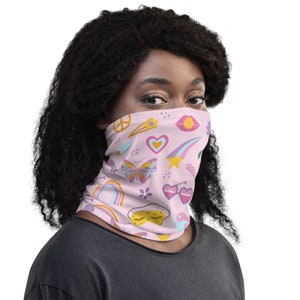 Puede incluir: Una mascarilla facial rosa con un patrón colorido de signos de paz, corazones, estrellas, mariposas y otros símbolos.