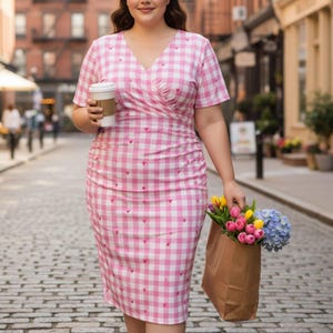 May include: A pink and white gingham print dress with small red hearts. The dress has a V-neck and short sleeves. A person is holding a coffee cup and a brown paper bag filled with colorful flowers, including tulips and hydrangeas.
