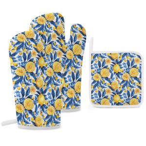 Puede incluir: Un juego de manopla y agarradera blancos con un estampado de limón y hojas azules. La manopla y la agarradera tienen un diseño repetido de limones amarillos y hojas azules sobre un fondo blanco. La agarradera es cuadrada con un borde blanco.