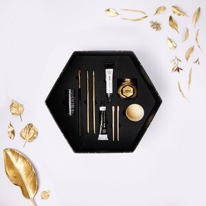 May include: A black hexagonal box with a variety of gold and black craft supplies, including paint, brushes, and a small jar of gold powder. The box is open and the supplies are arranged neatly inside.
