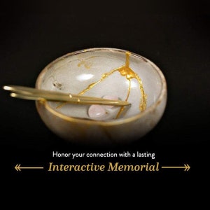 May include: A small, gray ceramic bowl with gold cracks and a pink stone inside. The bowl is sitting on a black surface. The text "Honor your connection with a lasting Interactive Memorial" is below the bowl.