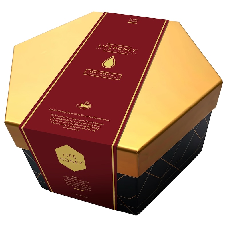 May include: A hexagonal gift box with gold and black geometric designs. A burgundy band wraps around the box, featuring the text "LIFEHONEY" and "NEWLYWEDS KIT". The box is designed for a wedding gift.