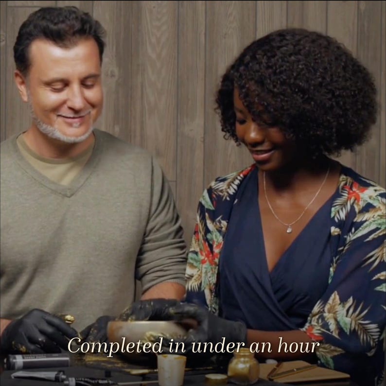 May include: Two people working on a craft project, wearing gloves. The image shows a woman wearing a blue dress and a floral patterned shawl, and a man wearing a green sweater. The text "Completed in under an hour" is visible at the bottom.