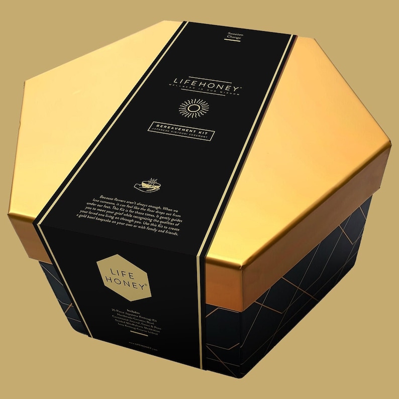 May include: A gold hexagonal box with a black label that says "LIFEHONEY" and "BEREAVEMENT KIT". The box is decorated with a sun and a gold honeycomb pattern.
