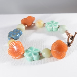 May include: A bracelet made with orange, blue, and green flower-shaped beads and copper wire. The bracelet has a toggle clasp.