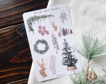 May include: A sheet of Christmas themed stickers with illustrations of a wreath, a deer, a Christmas tree, and a stocking. The stickers are on a white background and have the text "deck the halls" at the top.