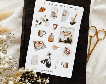 May include: A set of stickers featuring illustrations of a coffee maker, a croissant, a cat, a plant, a cup of coffee, a newspaper, a candle, and a mug. The stickers are on a white background and have the text "on a sunday morning" and "alwayslovelyco".