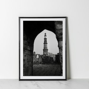 May include: A black and white photograph of a tall, slender tower seen through an archway. The tower is made of stone and has a pointed top. The archway is made of brick and is surrounded by other stone structures.