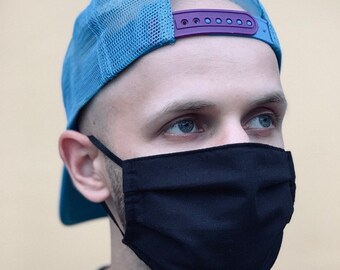 May include: A man wearing a blue mesh baseball cap with a purple strap and a black face mask.