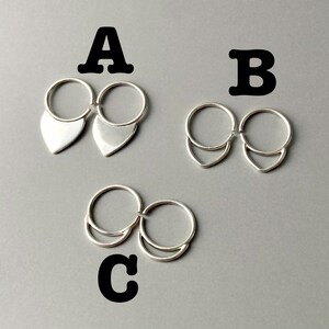 May include: Three pairs of silver earrings. The earrings are connected by a small ring. The first pair has a teardrop shape. The second pair has a curved shape. The third pair has a crescent shape. The earrings are on a gray background.