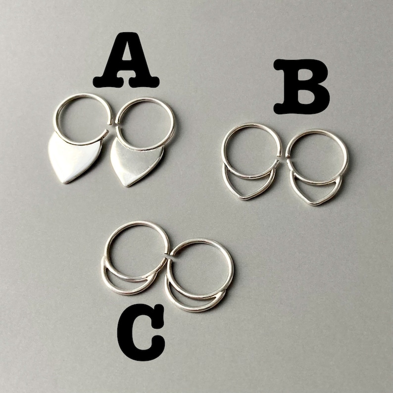 May include: Three pairs of silver earrings. The earrings are connected by a small ring. The first pair has a teardrop shape. The second pair has a curved shape. The third pair has a crescent shape. The earrings are on a gray background.