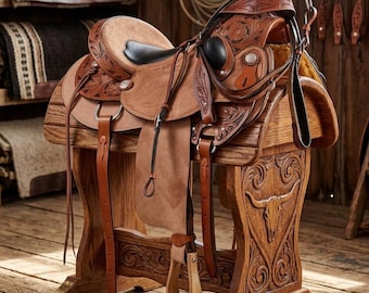 May include: A tan leather western saddle featuring intricate floral tooling, a smooth black seat, and silver conchos. The saddle includes matching leather stirrups and straps, resting on a carved wooden stand with a bull skull motif design.