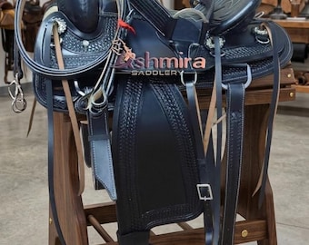 May include: A black leather western saddle featuring intricate basket-weave tooling, silver-toned conchos, and a matching headstall. The saddle displays the text "Kshmira SADDLERY" in orange and white lettering across the seat and side panels.