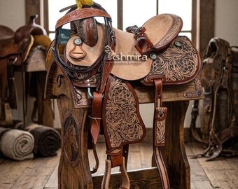 May include: A tan leather western saddle featuring intricate floral tooling and dark brown accents. The saddle includes a matching bridle with a yellow fuzzy accent on the crown piece and silver-toned hardware. The text Kashmira Saddlery is visible.