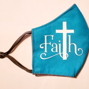 May include: A turquoise blue face mask with a white cross and the word "Faith" in a white cursive font.