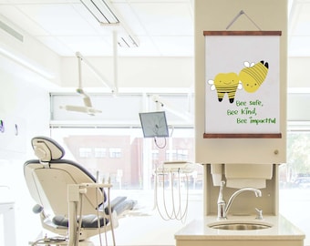 Puede incluir: Una oficina dental blanca con dos sillas y un lavabo. Una impresión enmarcada con un dibujo animado de un diente y una abeja dice "Bee safe, Bee kind, Bee impactful".
