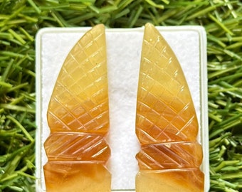 May include: A pair of carved amber earrings in the shape of a pointed, geometric design. The earrings are a light yellow color with a darker amber color at the bottom.