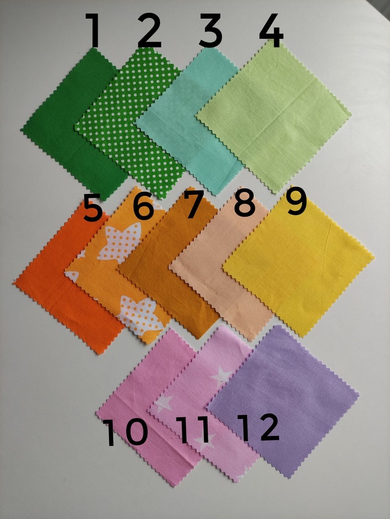 May include: Twelve fabric squares in various colors and patterns, numbered 1 through 12. The squares are arranged in three rows, with four squares in each row. The squares are all the same size and have a scalloped edge.