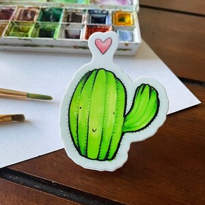 May include: A green cactus with a smiling face and a pink heart on top. The cactus is drawn in a cartoon style and has a white background.