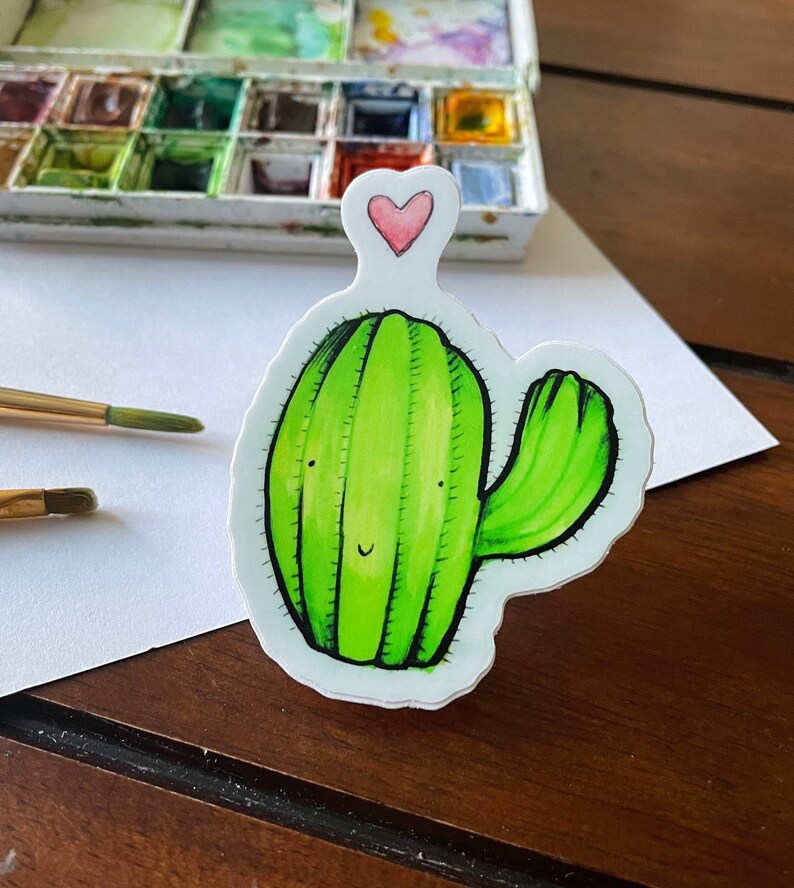 May include: A green cactus with a smiling face and a pink heart on top. The cactus is drawn in a cartoon style and has a white background.