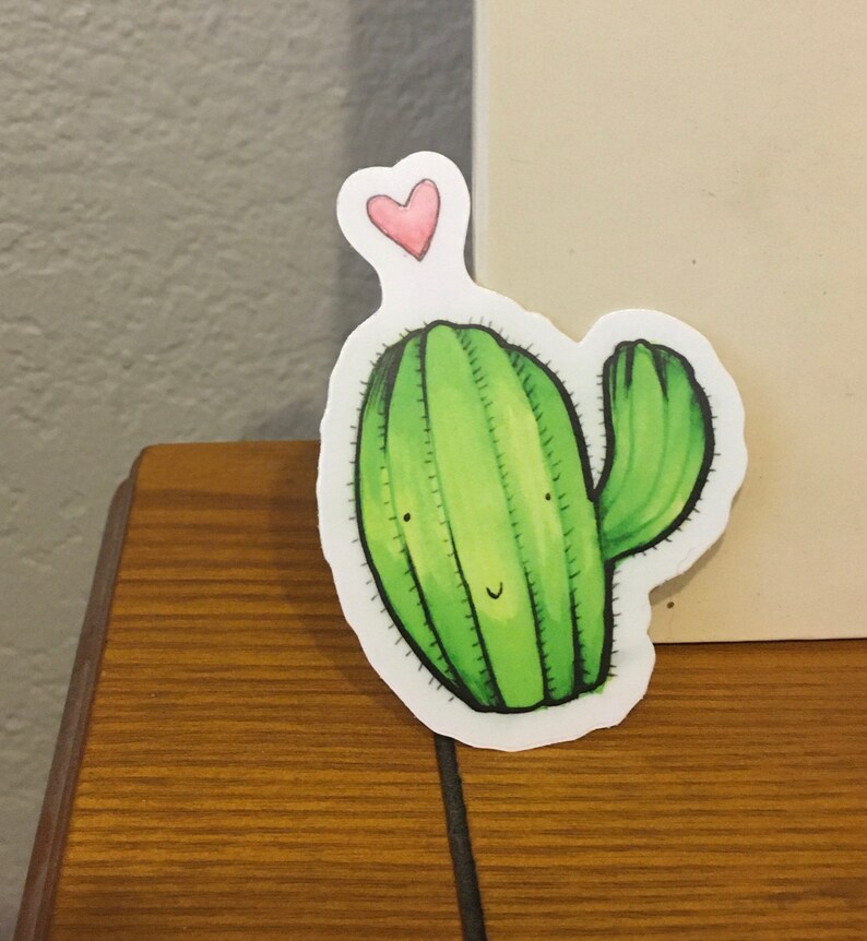 May include: A green cactus with a pink heart on top. The cactus has a smiling face and a single arm.