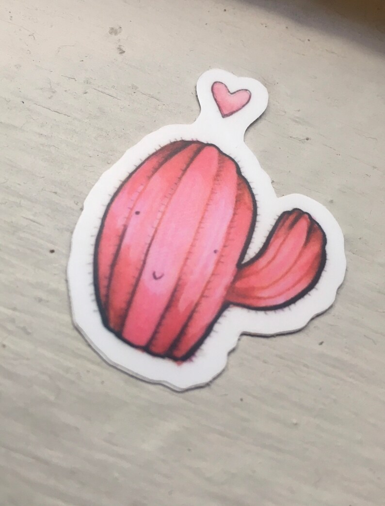 Pode incluir: Um cacto rosa com um rosto sorridente e um pequeno cora&ccedil;&atilde;o acima dele. O cacto tem um &uacute;nico bra&ccedil;o que se estende para o lado.