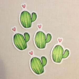 May include: Five green cactus stickers with pink hearts on top. Each cactus has a smiling face and a single arm.