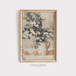 May include: A framed vintage painting of a white pitcher filled with white flowers and four lemons on a white tablecloth. The painting is in a light wood frame.