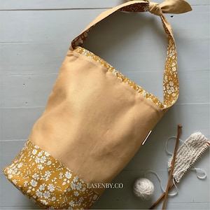 May include: A beige canvas tote bag with a floral print lining. The bag has a single strap and the brand name "LASENBY.CO" is printed on the bottom.
