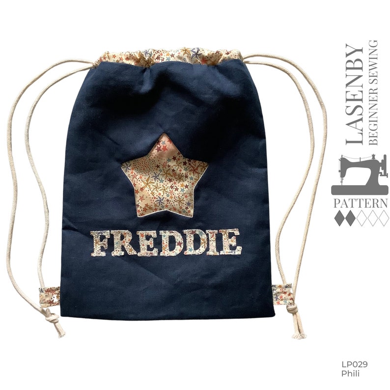 May include: A navy blue drawstring bag with a star-shaped patch and the name "FREDDIE" embroidered on the front. The bag has white drawstrings and a white background on the star patch.
