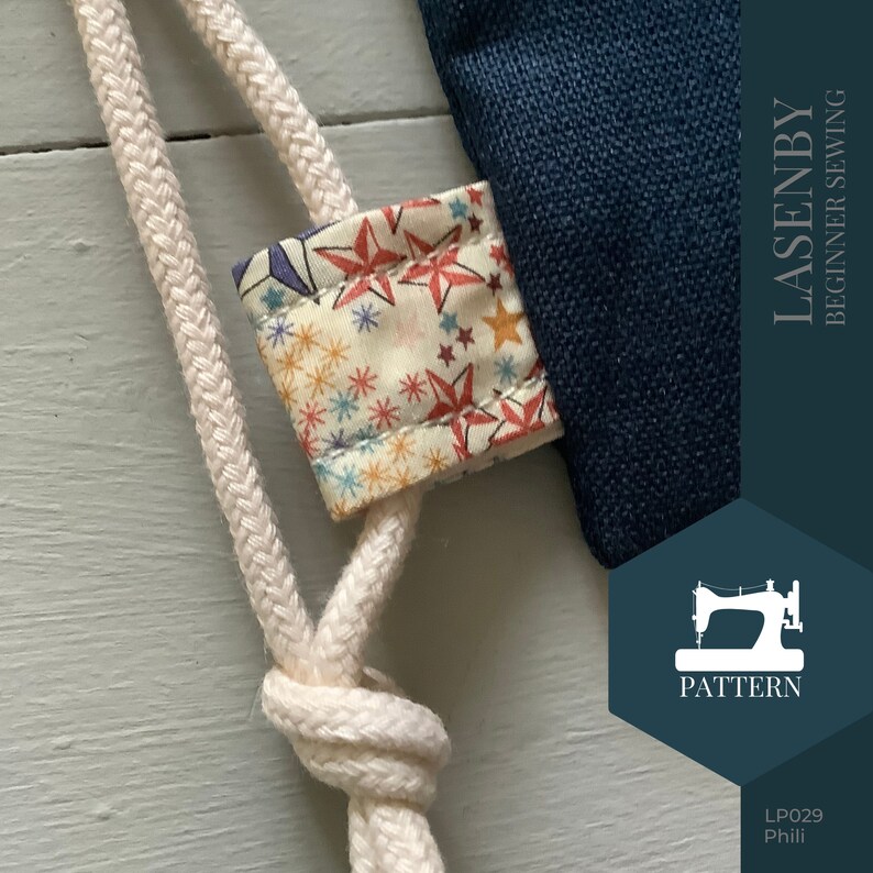 May include: A close-up of a white drawstring bag with a star-patterned fabric lining. The bag is made of a dark blue canvas material and has a white drawstring closure. The bag is labeled "LASENBY BEGINNER SEWING PATTERN LP029 Phili"