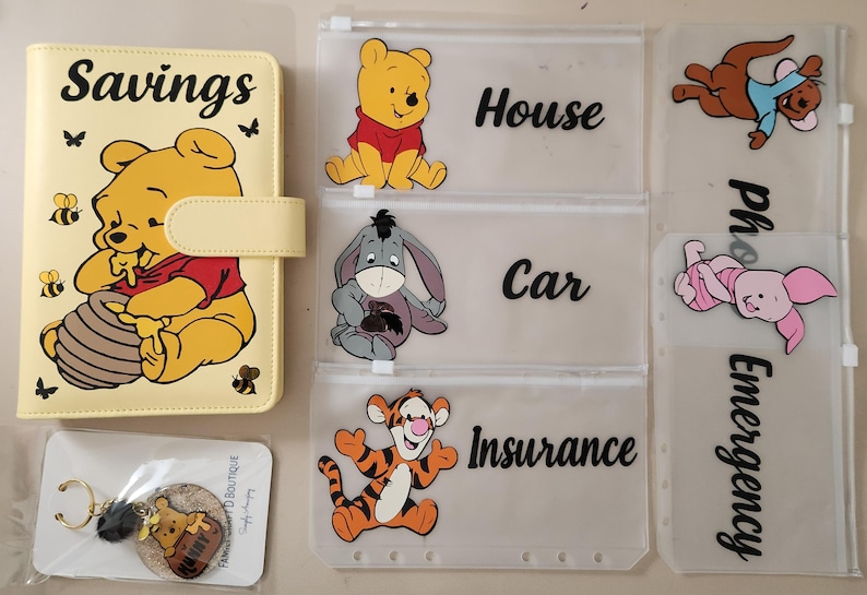May include: A yellow A6 binder with a Winnie the Pooh graphic and the word Savings, accompanied by five translucent zipper pouches featuring Winnie the Pooh, Eeyore, Tigger, Roo, and Piglet with labels for House, Car, Insurance, and Emergency.