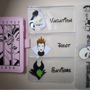 May include: A pink budget binder with the words "PERFECTLY WICKED" and illustrations of Disney villains. Clear plastic envelopes are labeled "Vacation," "Rent," "Savings," and "Bills/Miscellaneous," each with villain graphics.
