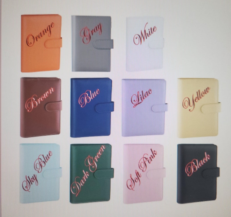 May include: A collection of eleven rectangular planners with textured covers and side closure tabs. Each planner features a color name in cursive script: Orange, Gray, White, Brown, Blue, Lilac, Yellow, Sky Blue, Dark Green, Soft Pink, and Black.