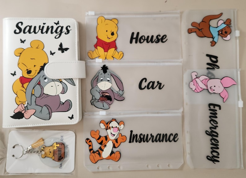 May include: A white A6 binder with a Winnie the Pooh and Eeyore graphic and the word Savings, three translucent zipper pouches labeled House, Car, and Insurance with character graphics, and a keychain with a Winnie the Pooh charm on a card.