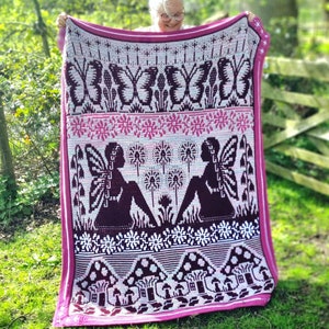 May include: A pink and purple crochet blanket featuring a fairy and butterfly design. The blanket has a repeating pattern of fairies, butterflies, dandelions, and mushrooms.