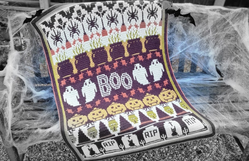 Puede incluir: Una manta de ganchillo de Halloween con un esquema de colores morado, naranja, blanco y verde. La manta presenta una variedad de dise&ntilde;os de tem&aacute;tica de Halloween, incluyendo fantasmas, calabazas, murci&eacute;lagos y l&aacute;pidas. La manta est&aacute; escrita "BOO" en el centro.