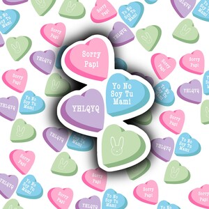 May include: A collection of heart-shaped candy conversation hearts with various messages in Spanish. The messages include "Yo No Soy Tu Mami" and "Sorry Papi". The hearts are in shades of pink, blue, green, and purple.