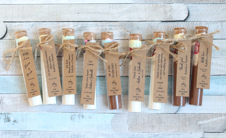 May include: Ten small glass test tubes filled with hot chocolate mix and tied with twine. Each tube has a brown paper tag with a personalized message, such as "Let love warm your heart" and "Thank you for warming our hearts".