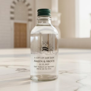 May include: Clear glass bottle with a green cap, filled with liquid. The bottle has a printed design of a building and text that reads "A GIFT OF ZAM ZAM AMEEN & AROOJ 22.12.2025 THE PUREST OF WATERS FROM US TO YOU."