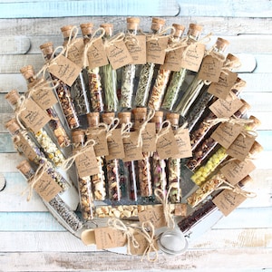 May include: An assortment of tea blends in clear glass vials with cork stoppers, arranged in a circular pattern. Each vial has a small tag with the tea type and a holiday greeting. The vials are tied with twine and presented on a wooden tray.