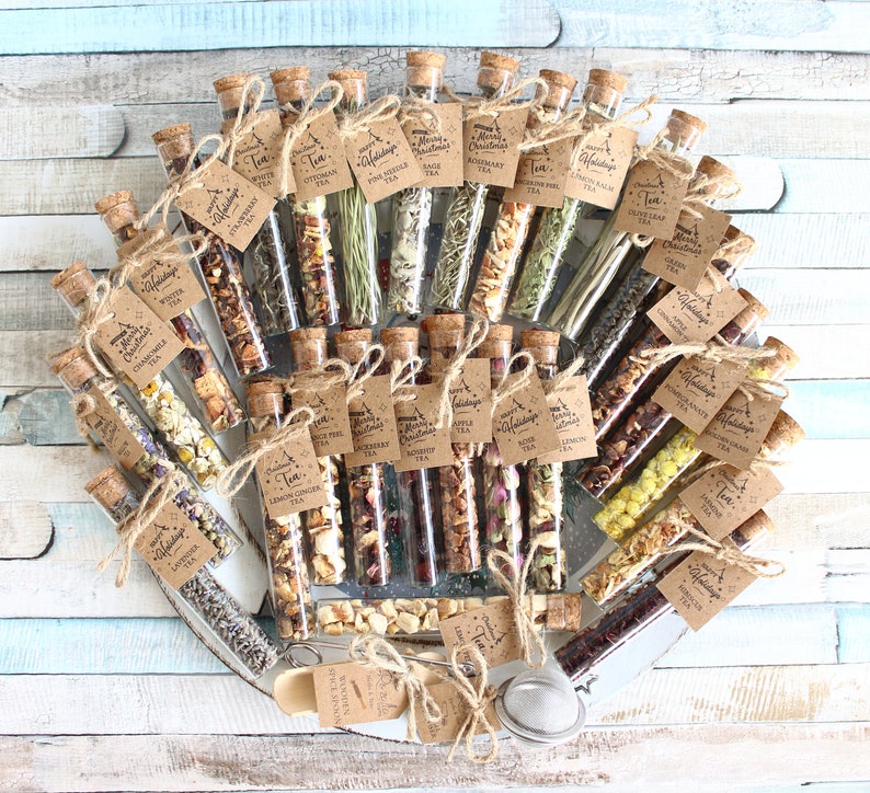 May include: An assortment of tea blends in clear glass vials with cork stoppers, arranged in a circular pattern. Each vial has a small tag with the tea type and a holiday greeting. The vials are tied with twine and presented on a wooden tray.