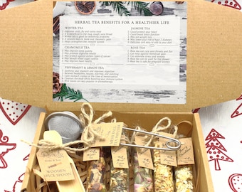 May include: A cardboard gift box containing five glass test tubes filled with various herbal teas, a metal mesh tea infuser, and a wooden spoon. The box lid features a printed chart titled Herbal Tea Benefits for a Healthier Life.