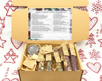 May include: A cardboard box filled with herbal tea products. The box contains glass tubes of tea, a mesh ball tea infuser, and a wooden spice spoon. A card lists herbal tea benefits. The text "Merry Christmas" is on the tubes.